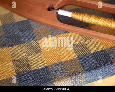 Woven checkered yellow and gray fabric on a hand loom with a wooden boat shuttle, selective focus. Weaving detail Stock Photo