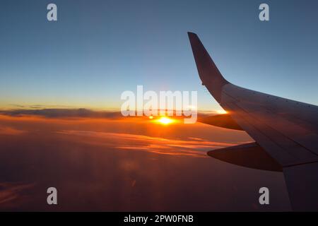 View from an airplane window showing a plane wing with orange sky at sunset Stock Photo