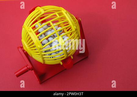 A jolly bright plastic basket with numbers to help with the Lottery, Lotto or just plain Bingo On  simple red background with copy space Stock Photo
