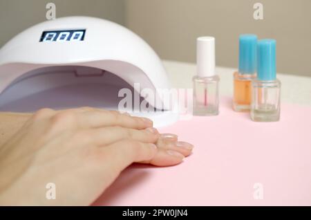 Close up female hands with beautiful trendy transparent manicure on white table background. Different modern tools for making long lasting gel polish Stock Photo