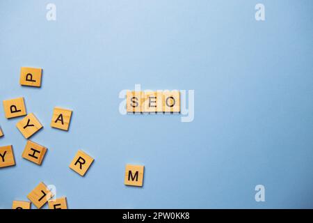 Wooden letters SEO are printed on a light blue background with many different wooden letters in the background Stock Photo