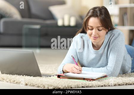 Teen studying lying on the floor taking notes at home Stock Photo