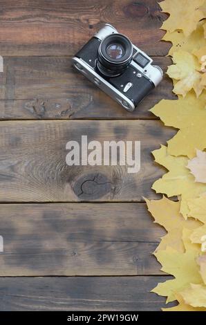 The old camera among a set of yellowing fallen autumn leaves on a background surface of natural wooden boards of dark brown color Stock Photo