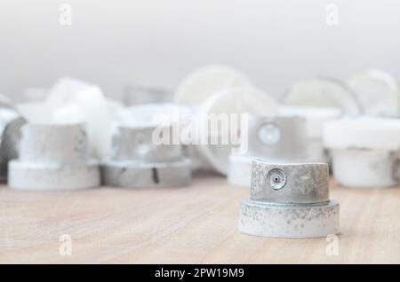 Several plastic nozzles from a paint sprayer that lie on a wooden surface against a gray wall background. The caps are smeared in chrome paint. The co Stock Photo
