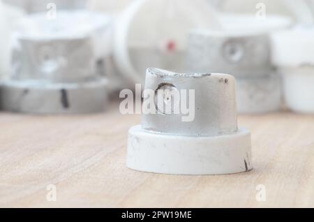 Several plastic nozzles from a paint sprayer that lie on a wooden surface against a gray wall background. The caps are smeared in chrome paint. The co Stock Photo