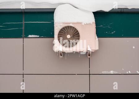 An outdoor air conditioner unit installed on the outer wall of a  building. Operation of the air conditioner in winter at low temperatures. Icicles an Stock Photo