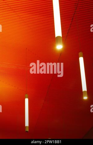 Intense orange ceiling with vertical light tubes. Modern architecture, interior. Stock Photo