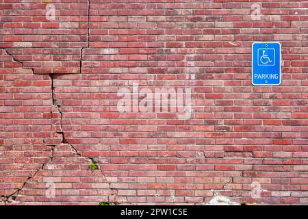 Handicapped parking sign on cracked brick wall Stock Photo