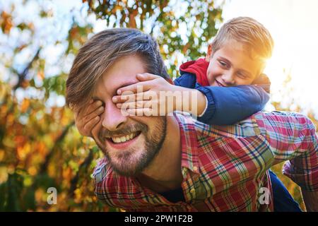 Cropped shot of an adorable young boy closing his fathers eyes while being piggybacked outside during autumn. Stock Photo