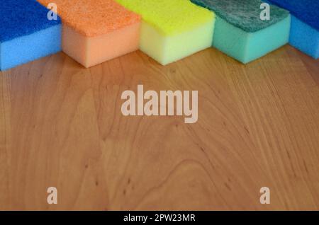 A few kitchen sponges lie on a wooden kitchen countertop. Colorful objects for washing dishes and cleaning in the house are ready for use Stock Photo