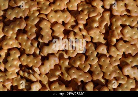 A huge bunch of salted biscuits of small sizes as a closed pattern or texture. A large amount of salted cracker in golden yellow tones Stock Photo