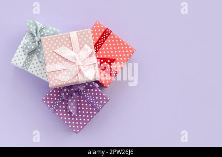 Pile of a small colored gift boxes with ribbons lies on a violet background. Minimalism flat lay top view. Stock Photo