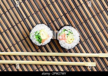 Sushi rolls and wooden chopsticks lie on a bamboo straw serwing mat. Traditional Asian food. Top view. Flat lay minimalism shot with copy space. Stock Photo
