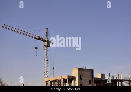 Working tall cranes inside place for with tall buildings under construction against a clear blue sky. Crane and building working progress with copyspa Stock Photo