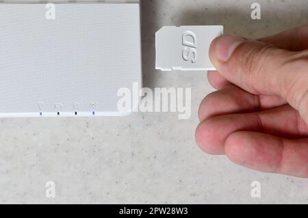 A male hand inserts a white compact SD card into the corresponding input in the side of the white netbook. Man uses modern technologies to store memor Stock Photo