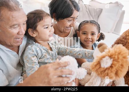 Closeup of to mixed race grandparents playing with their granddaughters and their teddy bears on the sofa at home. Family having a fun time at home. Stock Photo