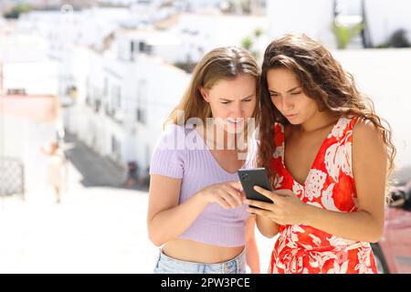 Two worried tourists checking smart phone online news on summer vacation Stock Photo