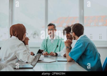 A group of multiethnic medical professionals including doctors, surgeons, and nurses are gathered in a hospital setting discussing patient care and Stock Photo