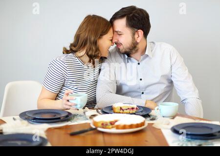 Woman cutting pie and man drinking beverage while having breakfast together at table in kitchen Stock Photo