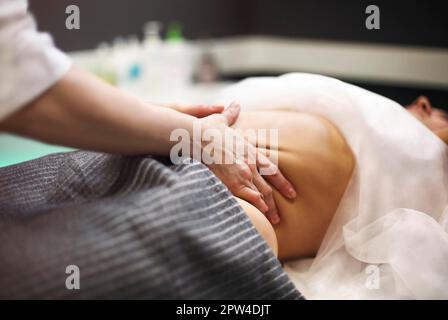 Partial view of masseur doing stomach massage to female on massage table Stock Photo