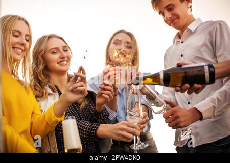Group of partying friends with flutes with champagne and bengal fire having fun on the party on the roof Stock Photo
