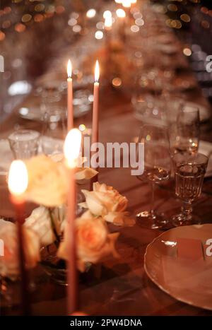 Burning candles and fresh flowers placed on banquet table near plates and glass goblets in evening Stock Photo