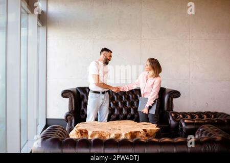 Positive man and woman in casual clothes shaking hands and smiling while striking deal during meeting in modern workplace Stock Photo