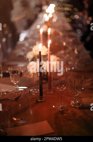 Burning candles and fresh flowers placed on banquet table near plates and glass goblets in evening Stock Photo