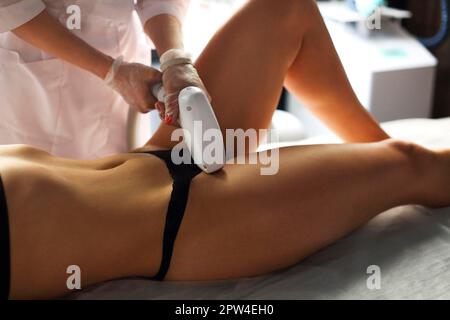 Cropped shot of beautician in medical uniform and gloves making laser hair removal procedure of bikini zone to young slender relaxed woman in black Stock Photo