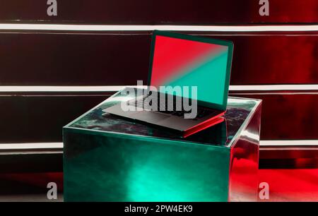 Modern opened laptop computer on creative designer metallic shiny cube with reflections of neon rays on notebook surface with blank mock up screen
