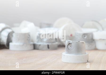 Several plastic nozzles from a paint sprayer that lie on a wooden surface against a gray wall background. The caps are smeared in chrome paint. The co Stock Photo