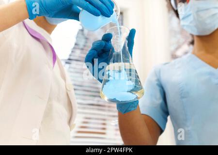 COVID-19 Testing Lab. Two women medical laboratory scientists colleagues wearing face masks working with test tubes, multi-ethnic graduate students Stock Photo