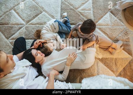 View from above of big family with two kids expecting new baby, waiting for third child. Pregnant mother, father, son and daughter spending time Stock Photo