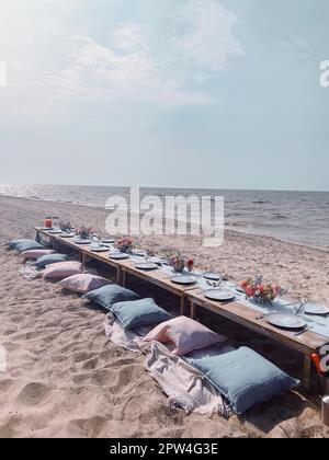 vertical photo of banquet table settings on beach with floral arrangements, dinnerware and cutlery, beautiful romantic wedding dinner gathering on Stock Photo