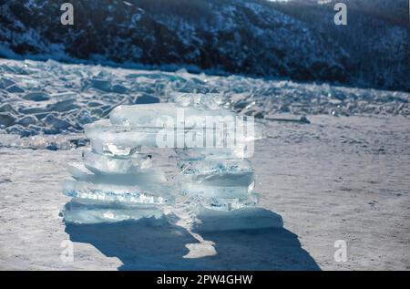 Pieces of ice lying on the ideal smooth ice of baikal with ice hummocks in the horizon. Sun is shining through the sides of ice cubes. Floes look Stock Photo