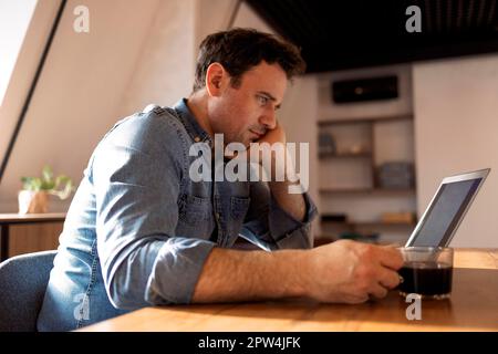 Smiling bearded caucasian businessman working on laptop at home office. Brunette student use computer distance learning surrounding video call Stock Photo