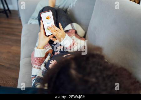 Back view of african american millennial woman holding smartphone, watching video, playing games, shopping, chatting on mobile app while sitting on Stock Photo