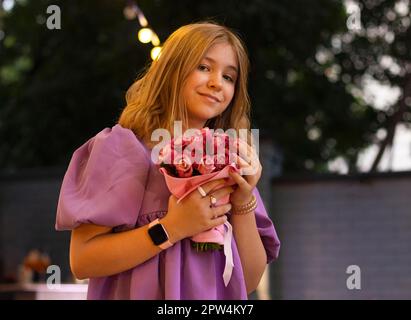 Cute teen girl with rose flowers. Child playing in summer garden. Kids gardening. Children play outdoors. Blond female with flower bouquet for Stock Photo