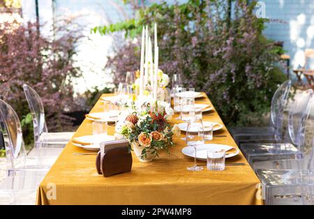 Wedding. Banquet. Chairs and a table for guests, decorated with candles, are served with cutlery and crockery and covered with yellow tablecloth. The Stock Photo
