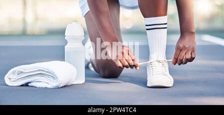 Tennis, athlete and sports feet tying her shoe laces ready for game, competition or training outdoor with water bottle gear. Fitness sneakers of black Stock Photo