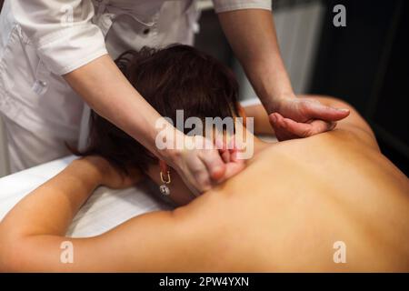 Faceless master giving massage of back and shoulder muscles to anonymous woman lying on table in spa salon Stock Photo