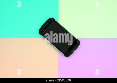 Black shock-proof smartphone lies on a pastel colored background. Modern technology concept. Minimalism flat lay. Blue, peach, lime and purple pastel Stock Photo