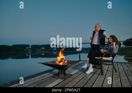 Couple is relaxing in the evening silence on the pier near the fire Stock Photo