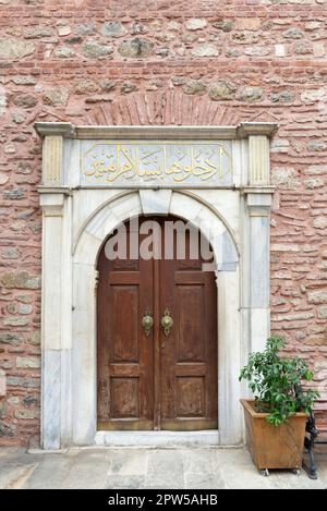 White marble decorated entrance of Arap Mosque, with wooden arched door, in red stone bricks wall, Karakoy, Beyoglu district, Istanbul, Turkey. Text a Stock Photo