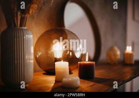 Round mirror on wooden shelf with two burning candles and small porcelain Buddha head reflected in corner of mirrored surface over concrete wall Stock Photo