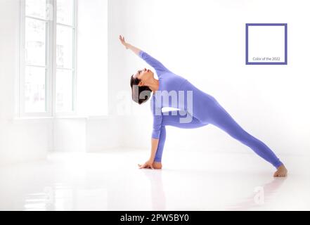 Young slender fit woman in violet long bodysuit performing yoga pose, isolated over white studio background. Healthy lifestyle, sport and fitness Stock Photo