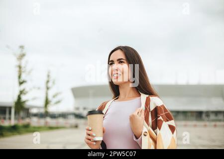 Cropped photo of pleased young woman with coffee to go cup standing outdoors, happy female wearing warm sweater holding hot drink and enjoying nice Stock Photo