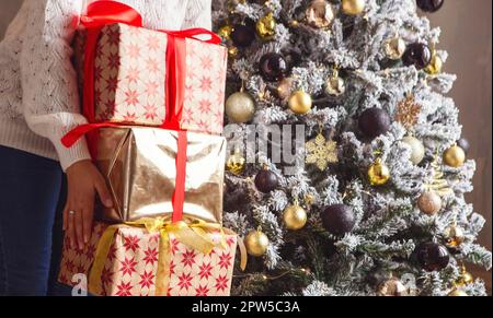 Cropped shot of woman holding stack of Xmas or New Year presents for family members and relatives while standing near decorated firtree Stock Photo