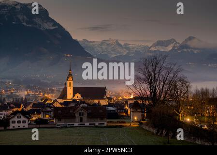 A church in the town of Schwyz in Switzerland in the twilight with fog and the mountains of the Alps Stock Photo