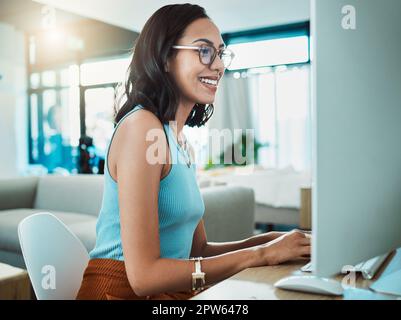 Social media agent with computer browsing online, typing and replying to customer or client emails in home office. Motivated, inspired and smiling cre Stock Photo
